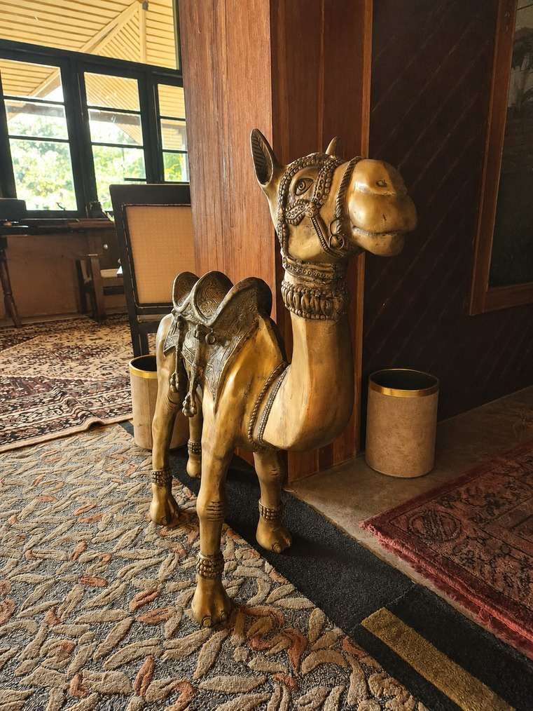 A gilded camel figure with an ornate saddle, standing on a patterned carpet.