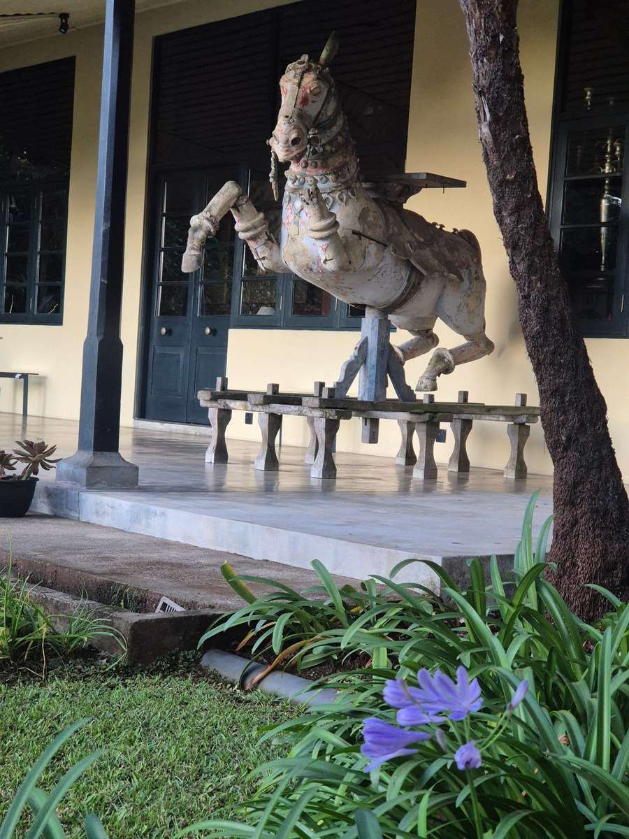 A weathered carved and painted horse, rearing on the verandah beside a tree.