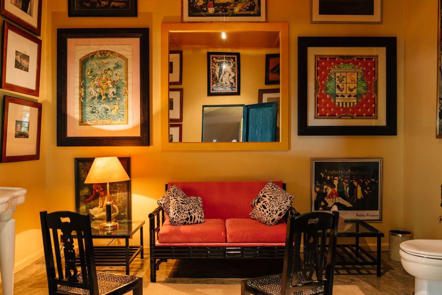 A yellow cloakroom hung salon-style with framed pictures, a red settee with leopard-print cushions and a Pablo Picasso poster.