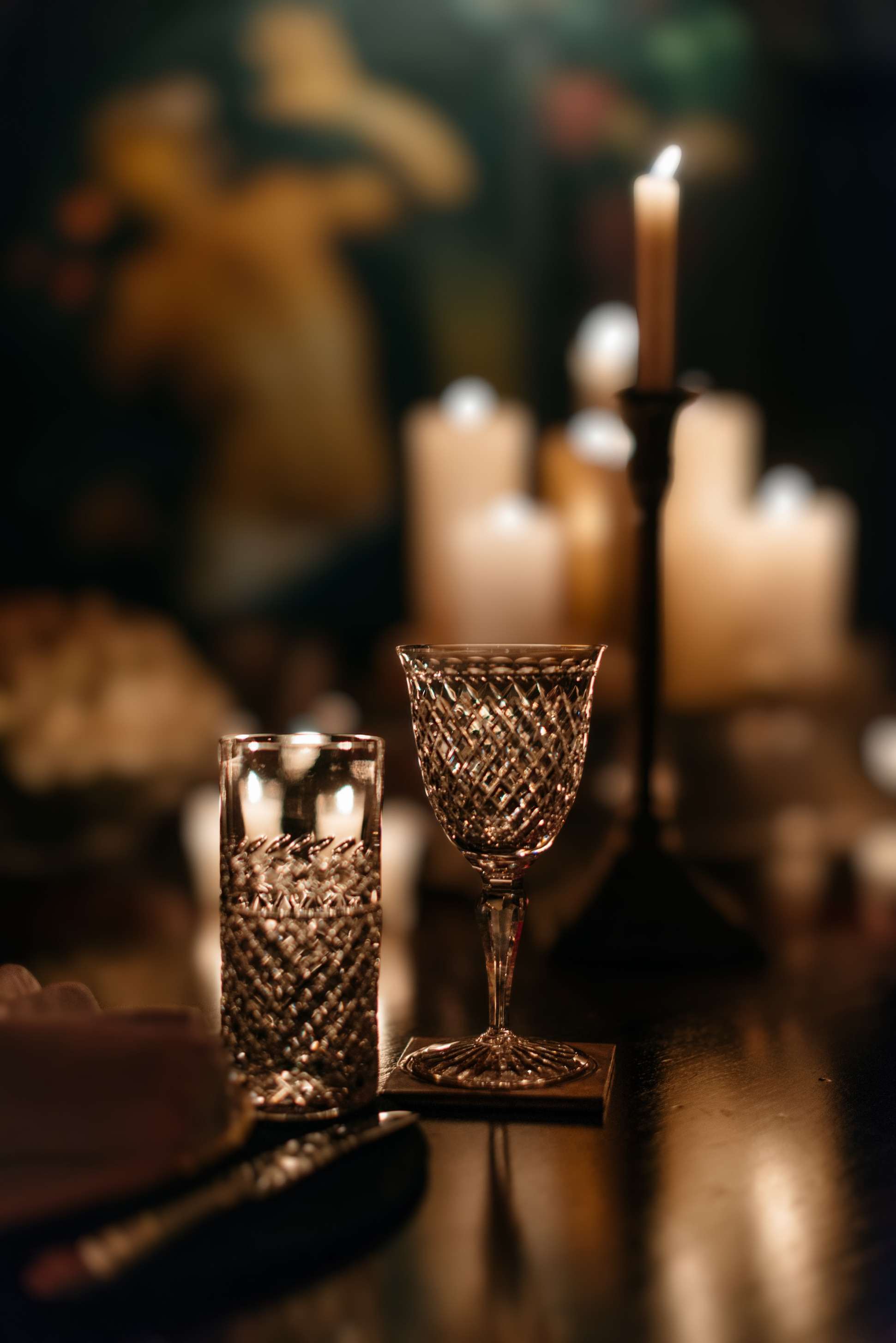 A cut-crystal glass on a dark table, candles glowing out of focus behind it.