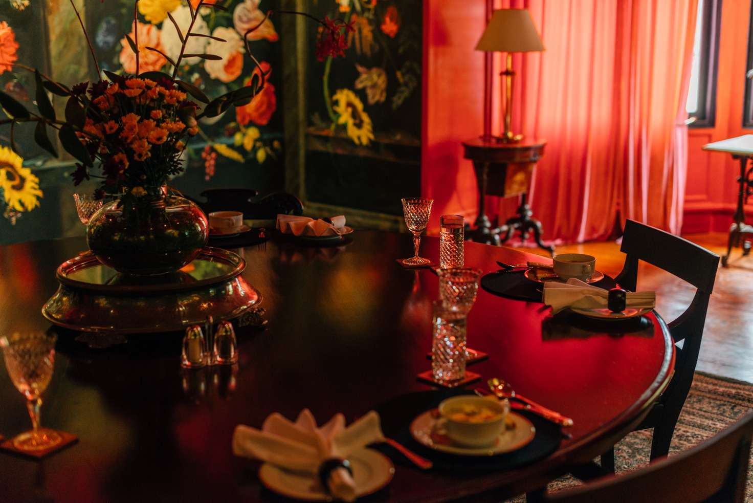 The dining table laid with crystal glasses, folded napkins and an urn of flowers, the painted panels behind.