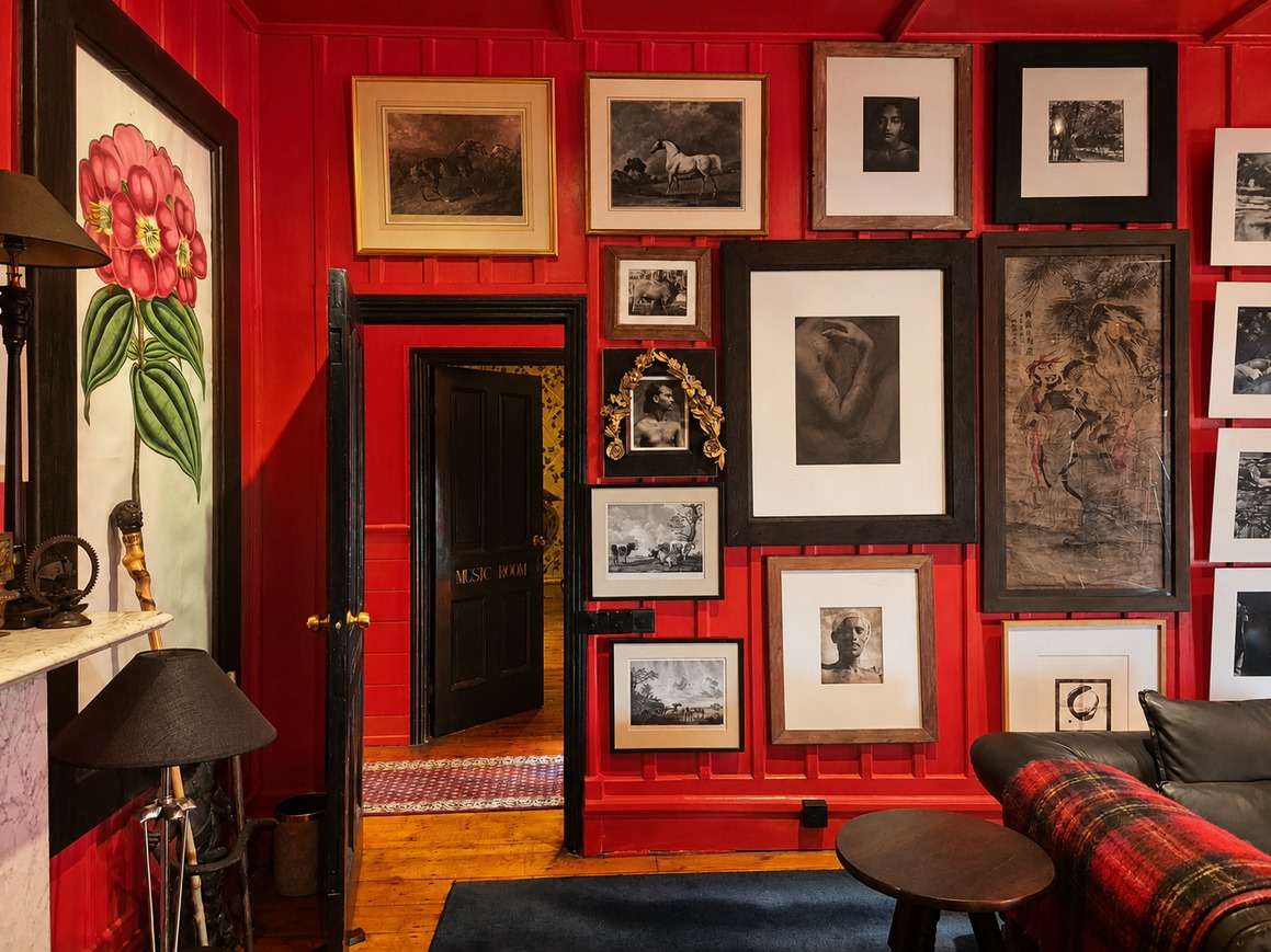 A red wall hung floor to ceiling with framed prints and photographs, beside an open black door.