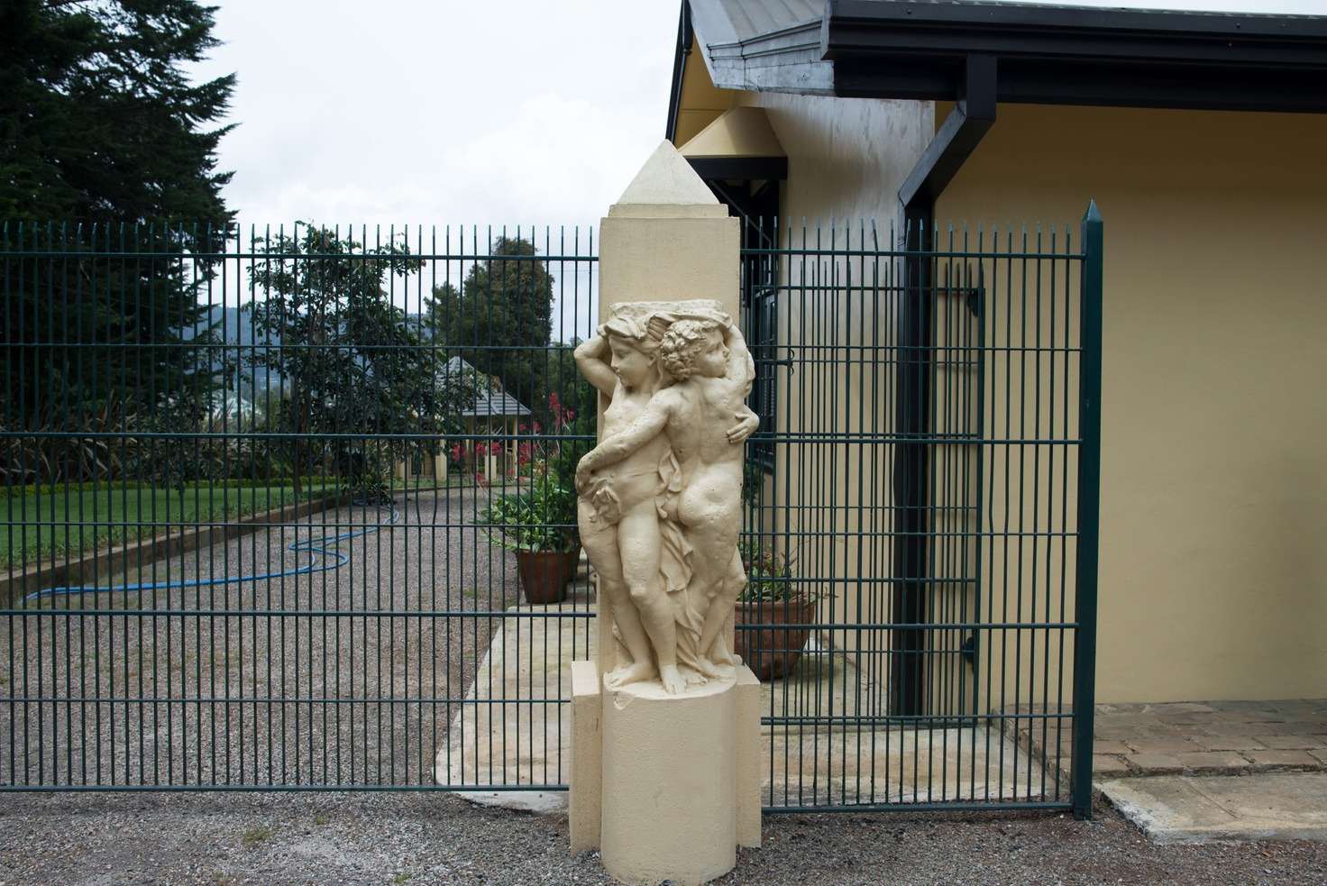A cream statue of two cherubs on a gatepost beside green railings.