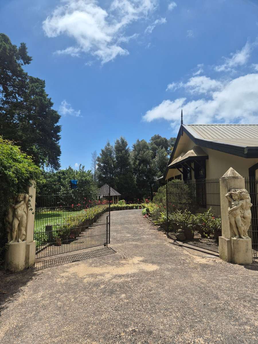 The open gates between two statue-topped pillars, the drive leading to the house.