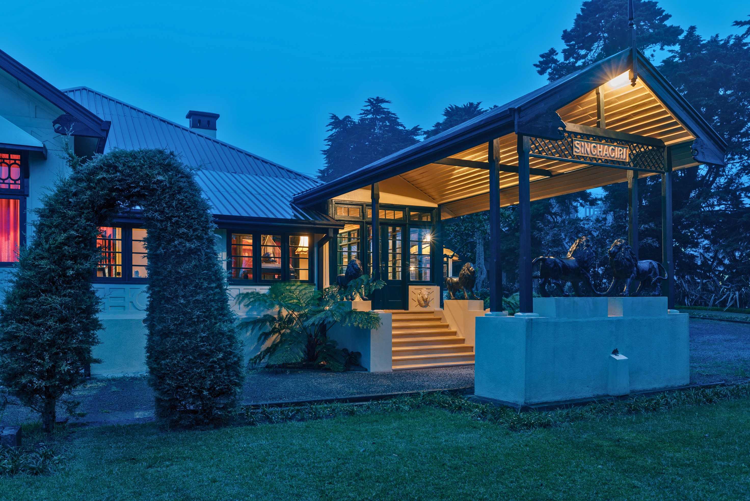 The entrance pavilion at dusk, lit from inside, with a pair of dark lion statues on a plinth before the steps.