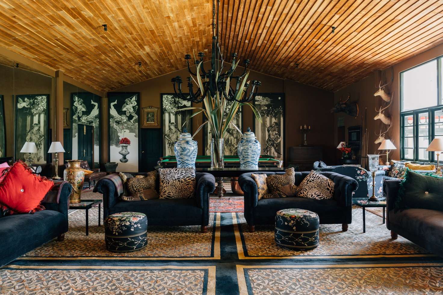 The great hall: a honey-coloured timber ceiling, a snooker table, blue-and-white ginger jars, navy sofas with leopard-print cushions and stag heads on the far wall.