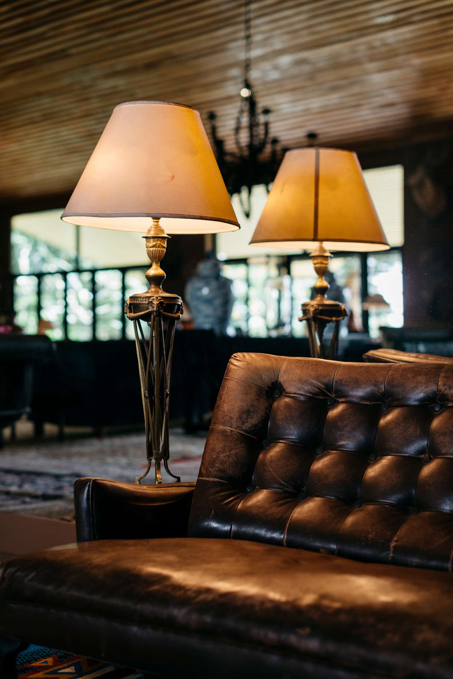Two brass lamps with parchment shades beside a tufted leather sofa.