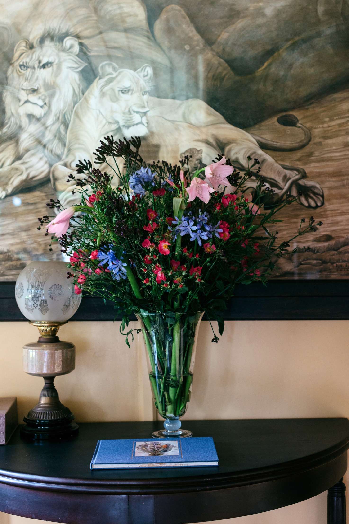 A large drawing of a lion and lioness above a vase of pink, red and blue flowers and an oil lamp.