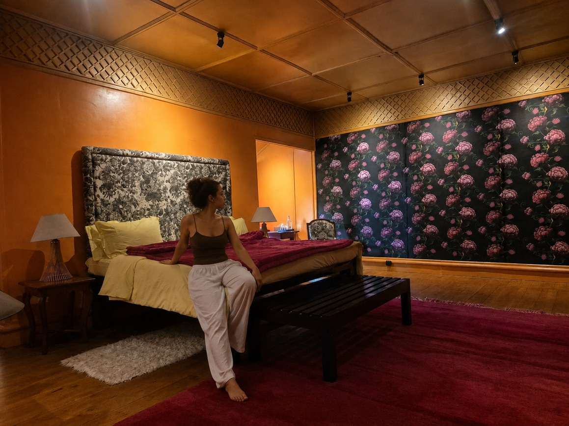 A bed with a toile headboard against dark floral wallpaper.