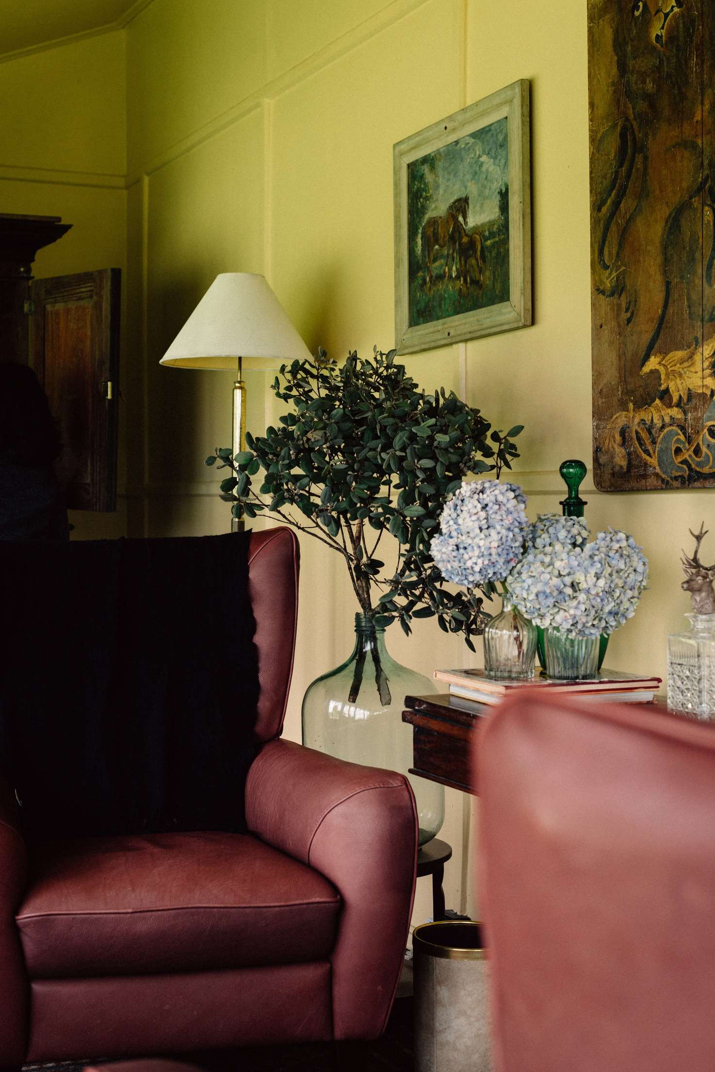 A red leather wing chair beside blue hydrangeas in glass vases and a stag figure.